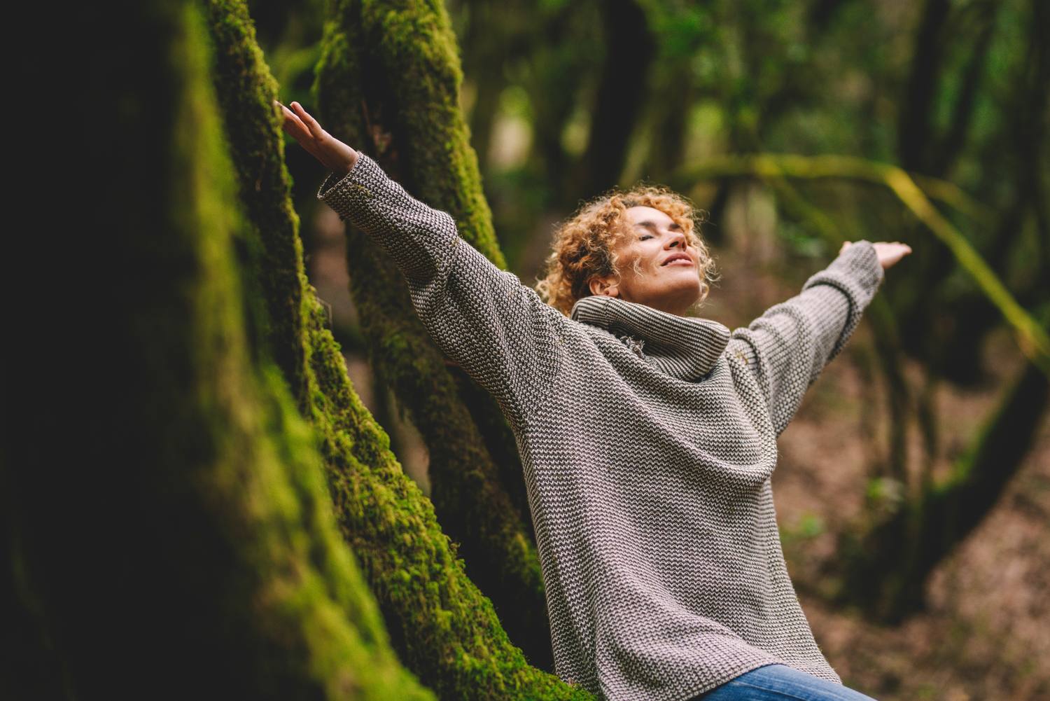 A woman with her arms open and eyes closed in a green forest